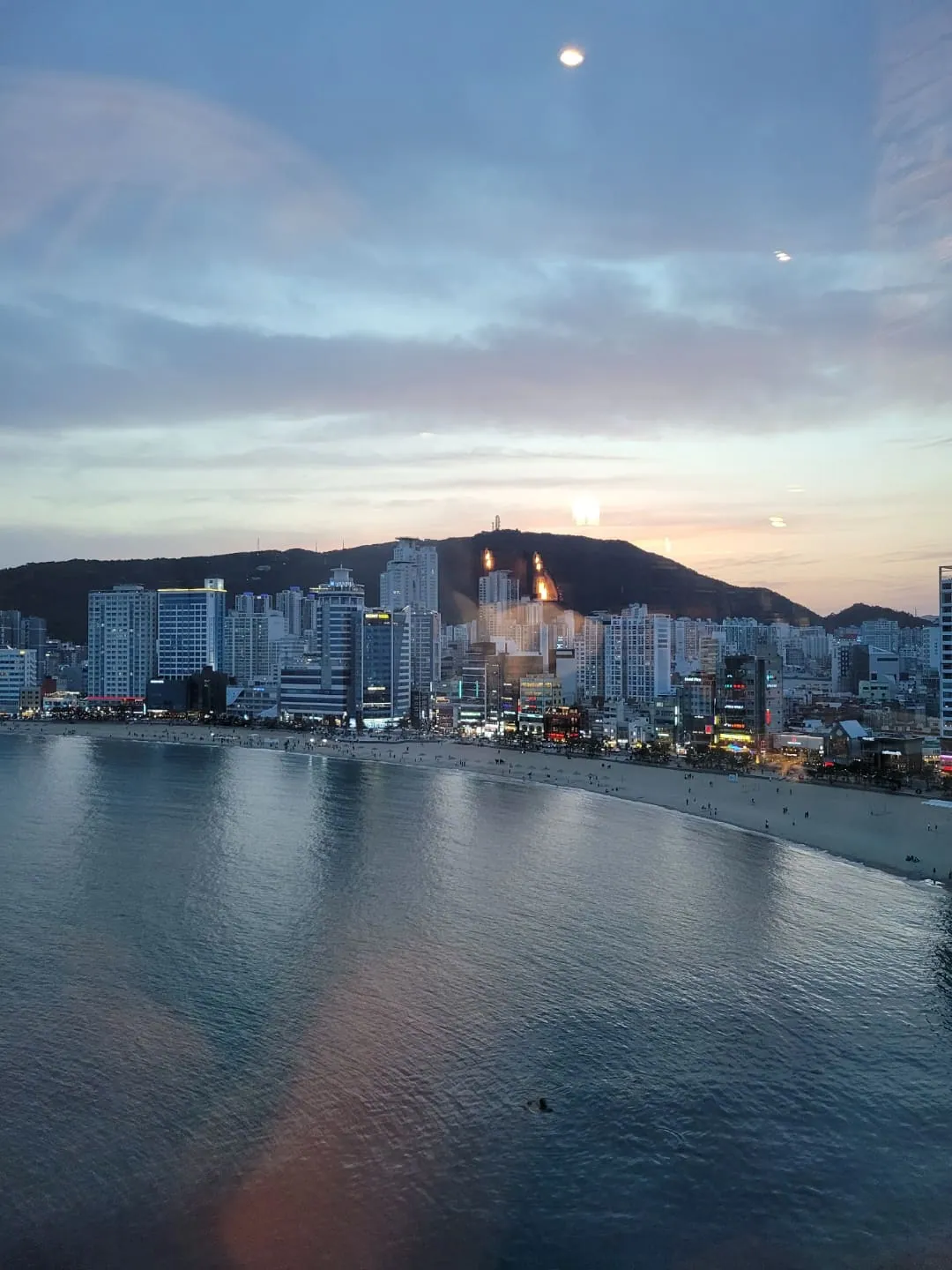 티앤북스 광안점 — Evening Gwangan Beach and bridge view photographed through the cafe window on the 8th floor; supplementary setting context only. Photo capture date unconfirmed; article published 2022-05-18T10:51:02+09:00.